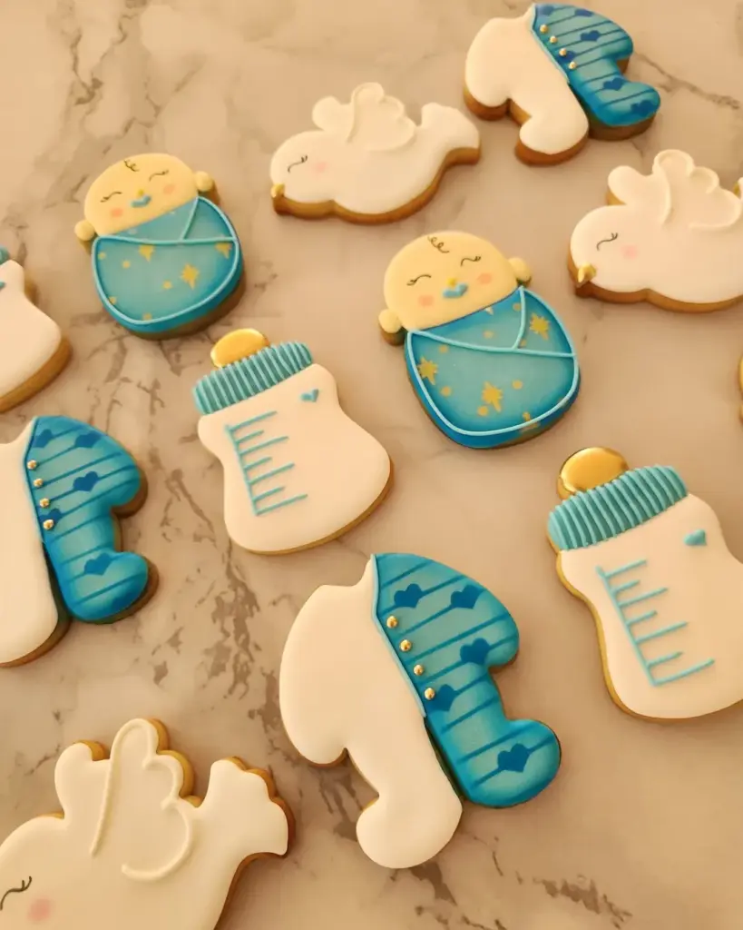 Galletas de baby shower con bebés envueltos, mamaderas y palomas en verde azulado y crema