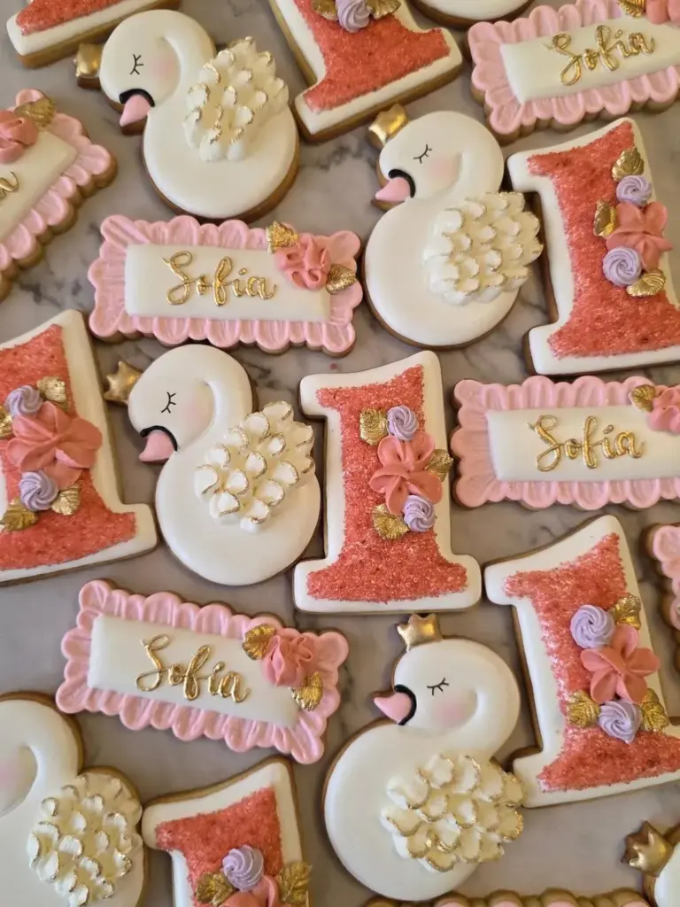 Galletas de primer cumpleaños con cisnes, número 1 y flores en coral y dorado